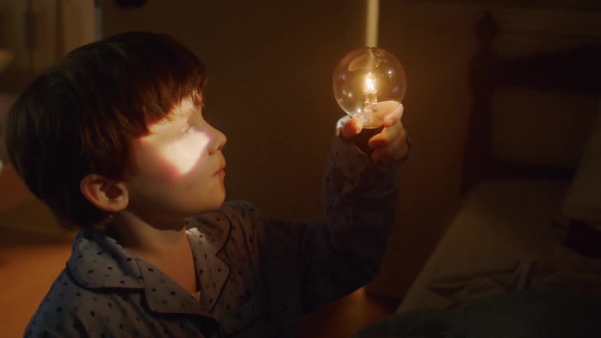 A boy holds up a glowing bulb in his bedroom at night