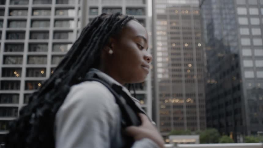 A girl wearing a backpack smiles as she walks through a city