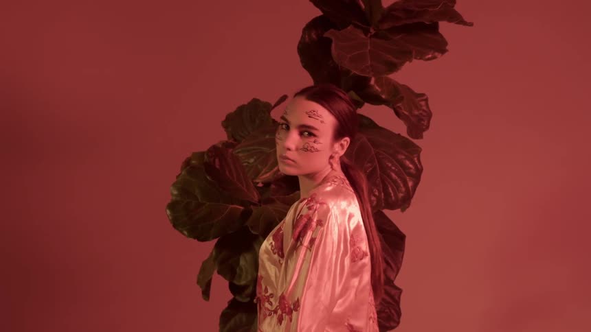 A woman with face paint poses in front of a plant