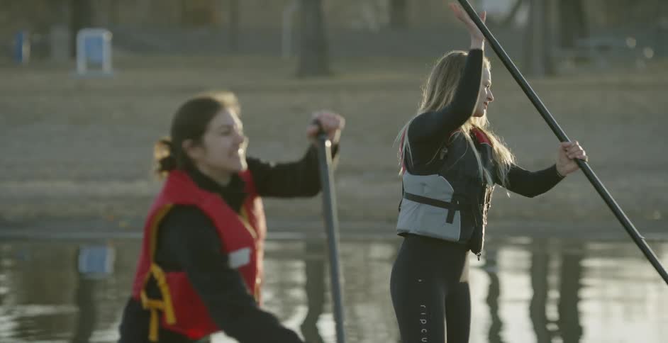 Two women are paddle boarding on a river in daylight