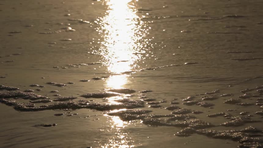 The waves slowly hit the shore at sunset