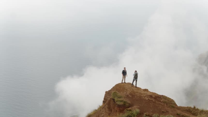 Two men stand on a mountain then one takes a photo of the other