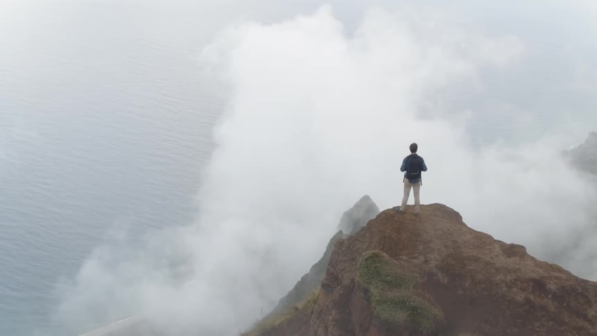 A man stands at the edge of the mountain top