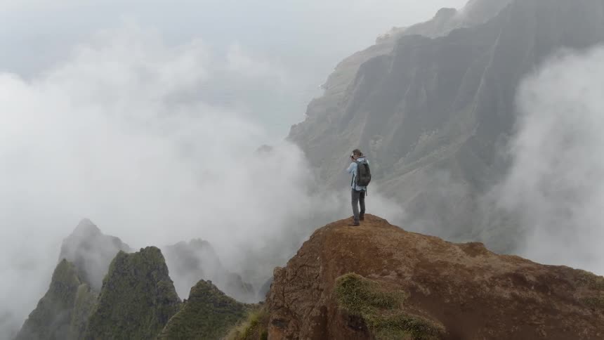A hiker stands on a mountain peak on a cloudy day