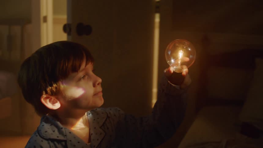 A boy holds up a glowing bulb in his bedroom at night