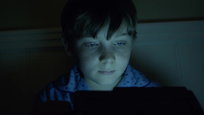 A boy is watching a monitor in the dark