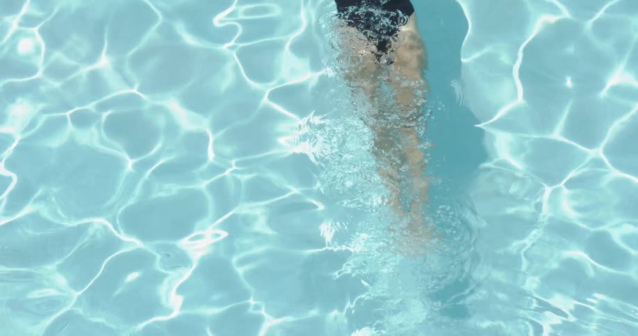 A swimmer is gliding underwater in a pool on a sunny day