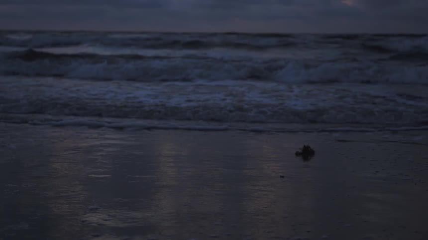Ocean waves are crashing in onto beach at dusk