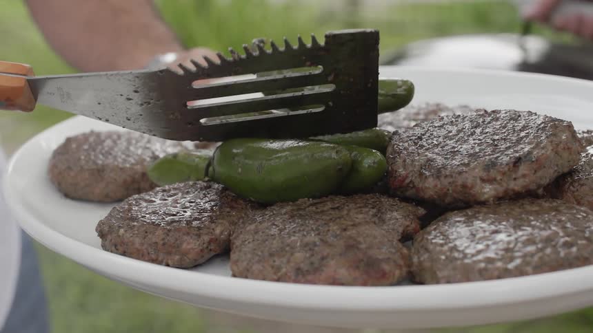 Person puts grilled jalapenos on a plate on top of some burgers
