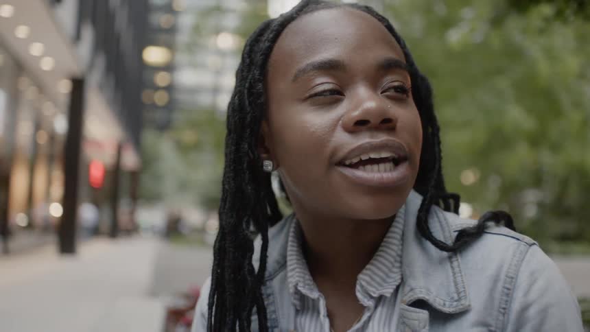 A woman nods her head while talking on a city sidewalk
