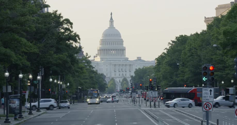 Cars drive on a street in front of a capitol building at sunrise