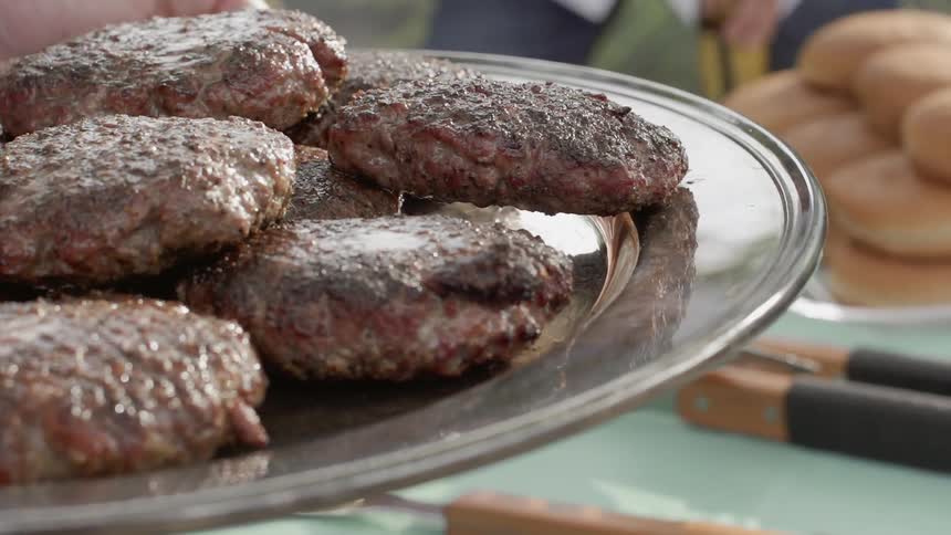 Pair of hands hold a plate of cooked meat patties