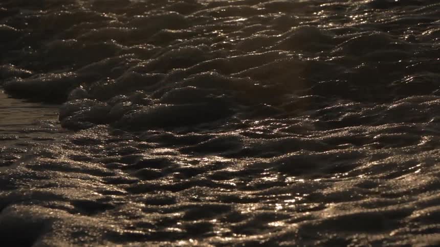 The waves crash against the shore at sunset