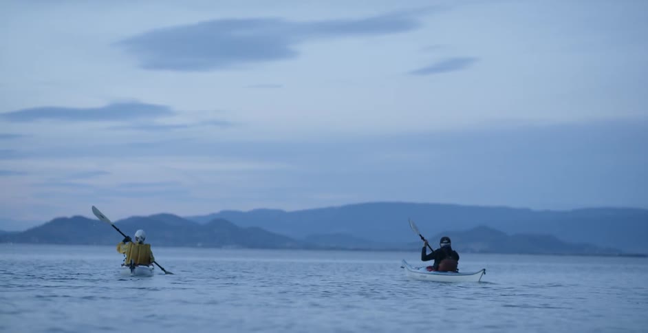 Two kayakers are paddling on a lake at dusk