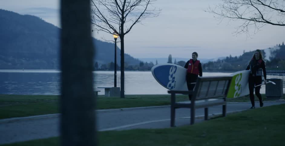 Two people carry paddle boards by the water