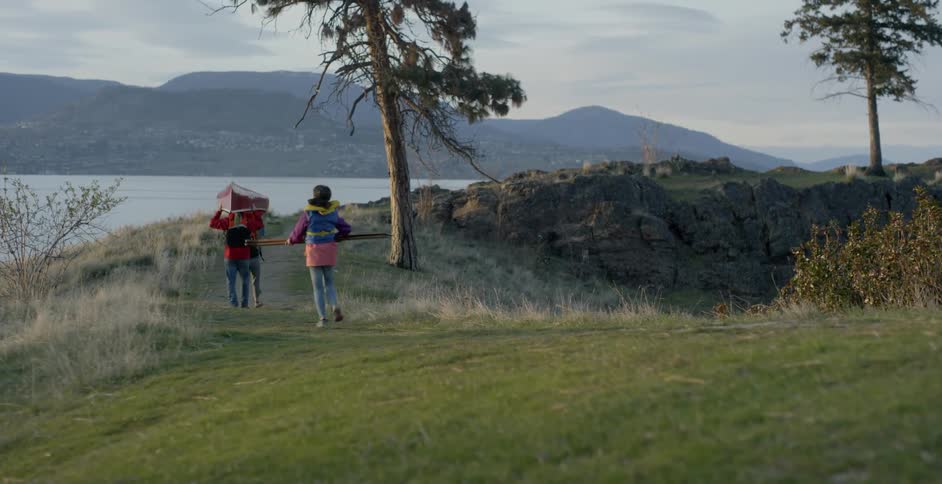 Young boy carries something as he runs towards two people carrying a canoe
