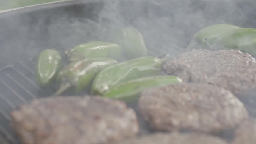 Hamburgers and peppers are cooked on a grill