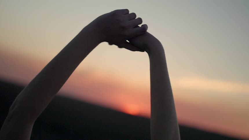 A woman is stretching her arms to the sky as she stands outside at sunset