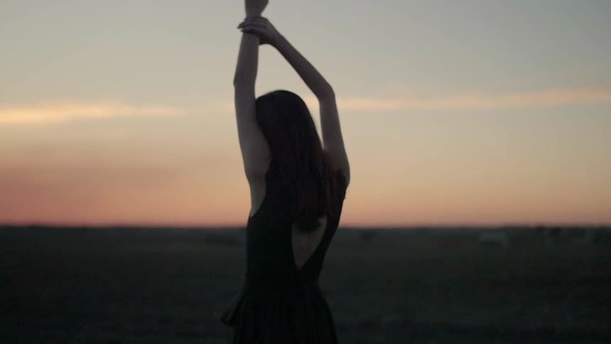 Woman stands and stretches her arms under the blue sky