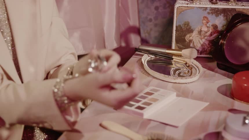 A woman sitting at a dressing table applies perfume
