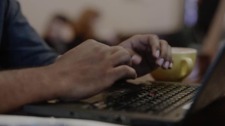 Man types on a laptop in a coffee shop