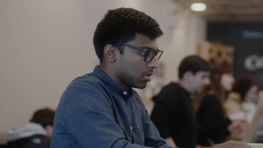 A man stands up and closes his laptop in a crowded coffee shop