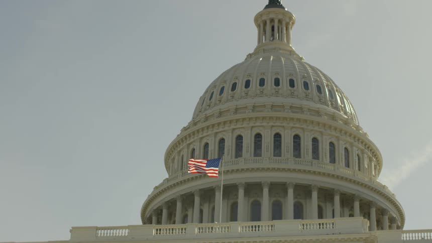 An american flag billows in front of a capitol building