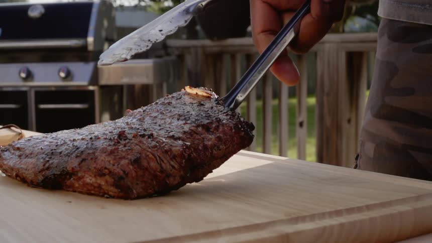 A cook is placing a slab of meat on a cutting board outside in daylight