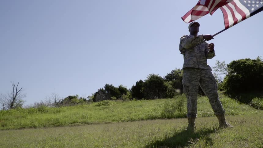 A soldier is standing outside on a sunny day waving a flag