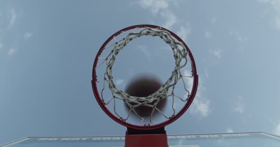 A basketball goes through a hoop in the daytime