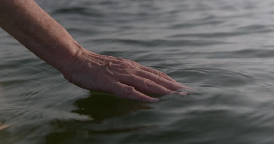 A hand skims the top of a lake