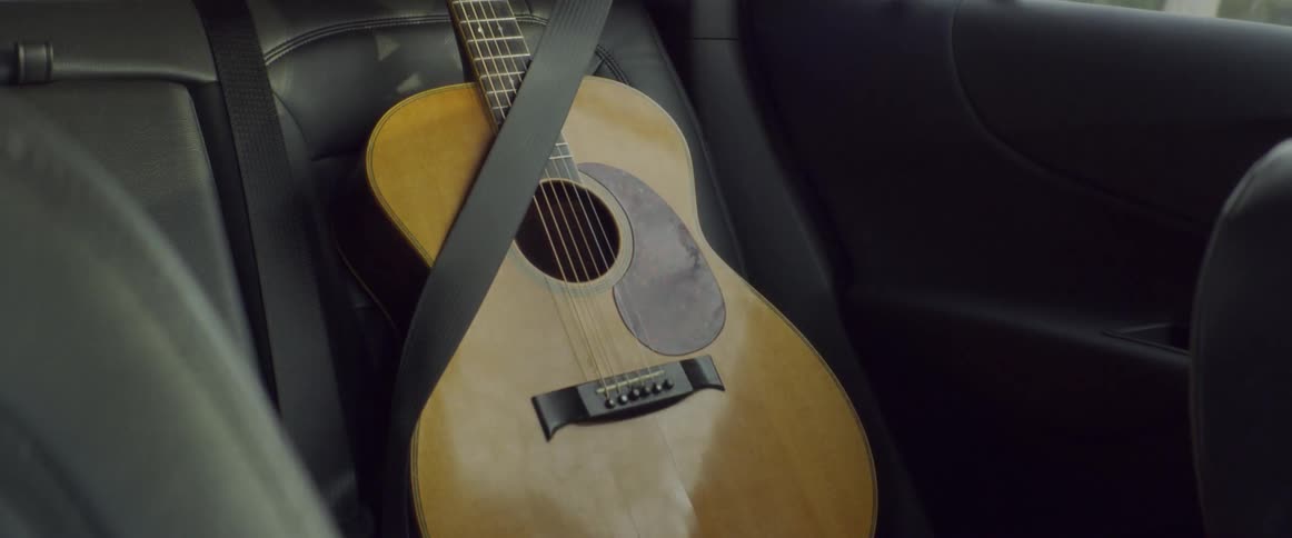 Guitar sits on a seat in a vehicle with a seat belt on