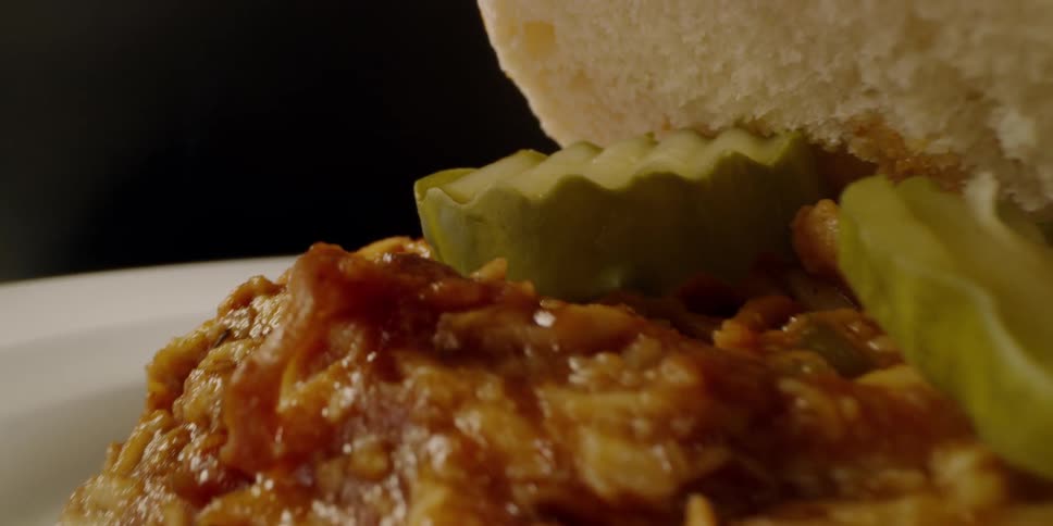 Shredded meat sandwich with pickles sits on a plate