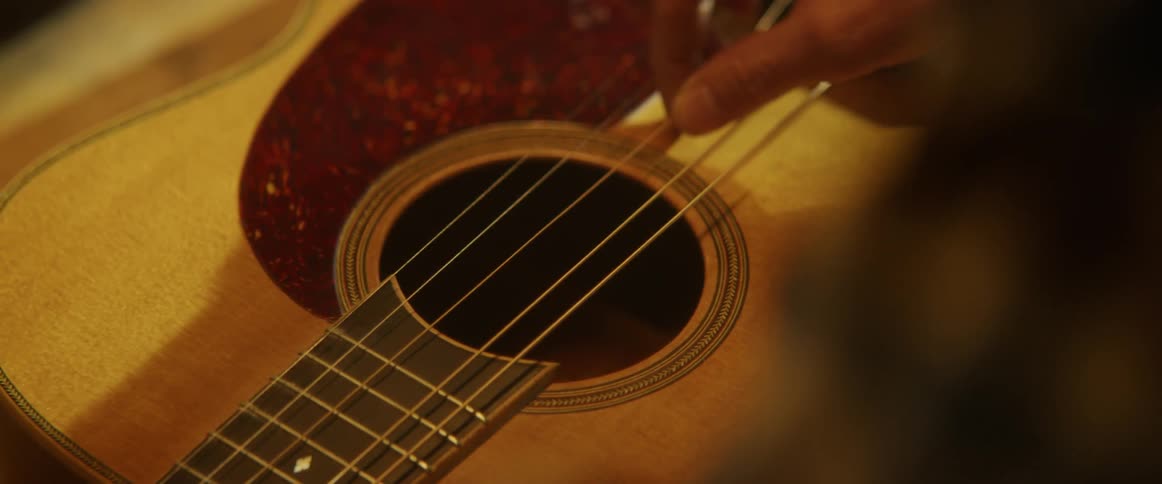 A man is stringing a guitar inside in daylight