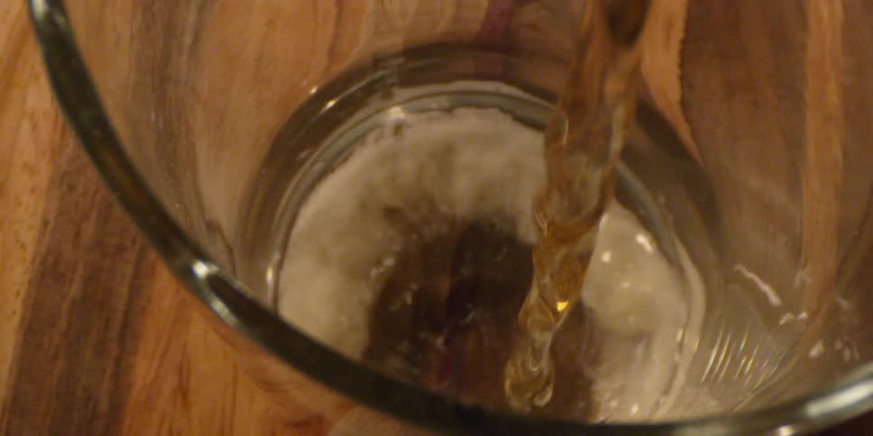 Fizzy liquid pours into a glass that is on a wood table