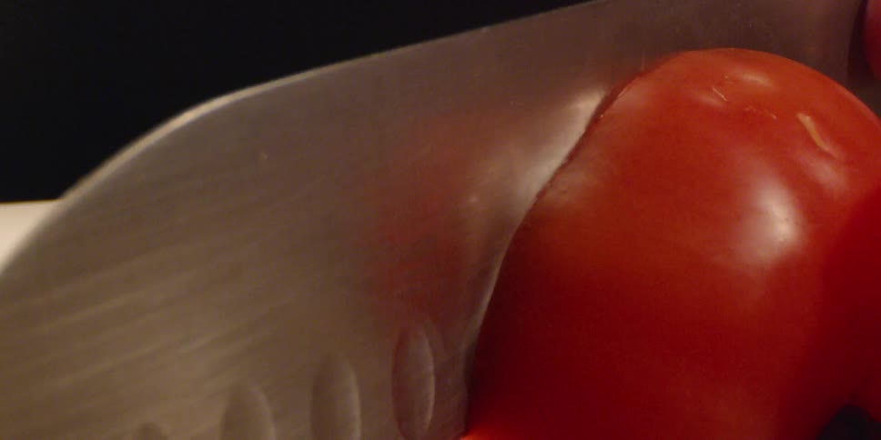 Large knife slices through a red tomato