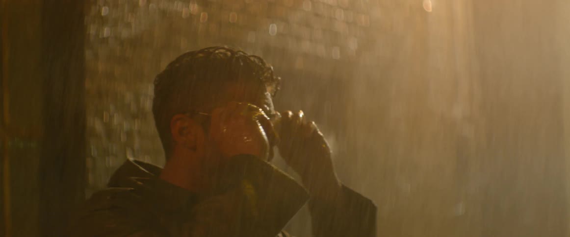 A man standing out in the rain wipes his glasses and looks around