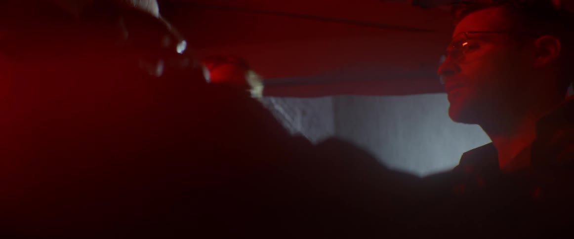 A man is being roughly escorted into a building on a rainy night