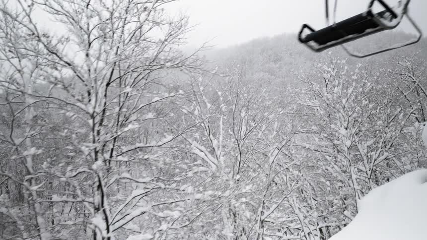 The ski lift is covered with snow as it moves