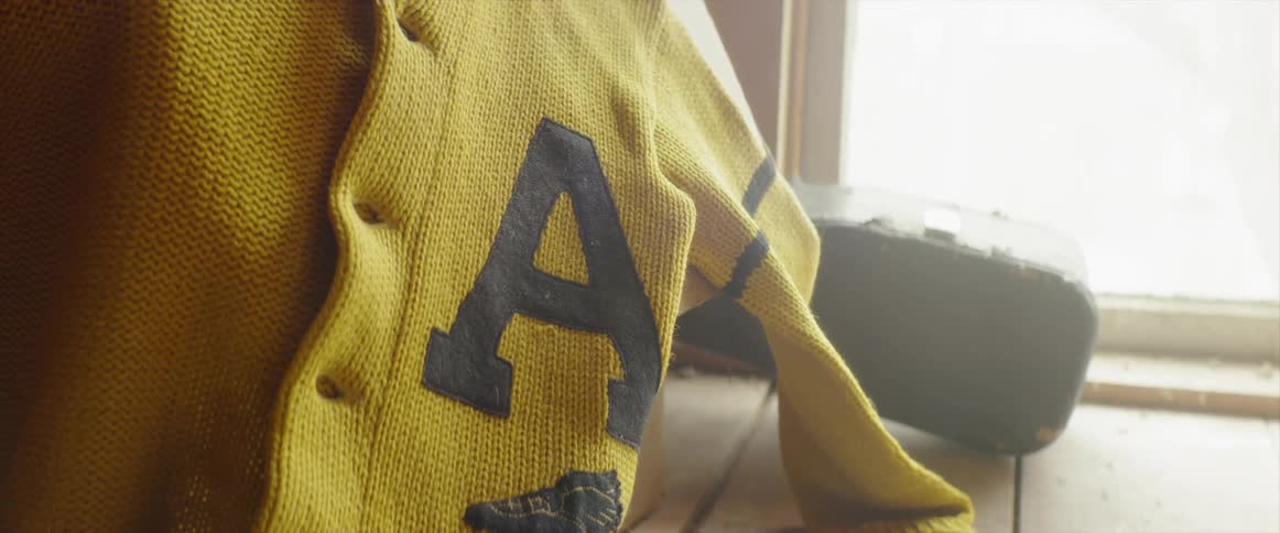 A letterman sweater is hanging near a window inside in daylight