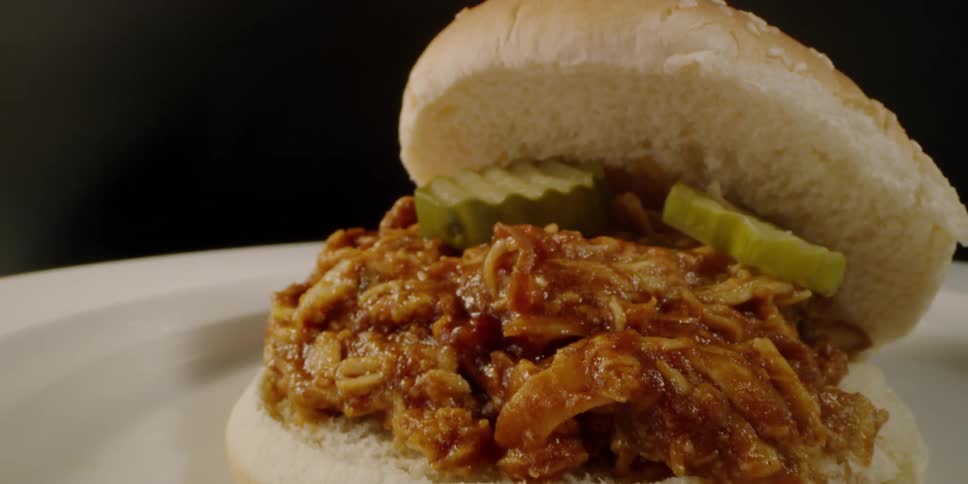 Pulled meat sandwich with pickles sits on a plate