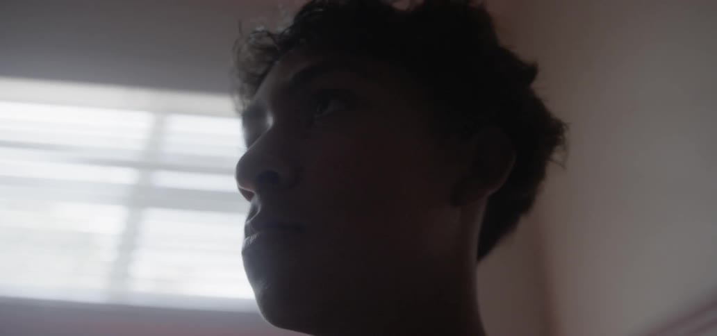 Teenage boy sits in a room in front of a window