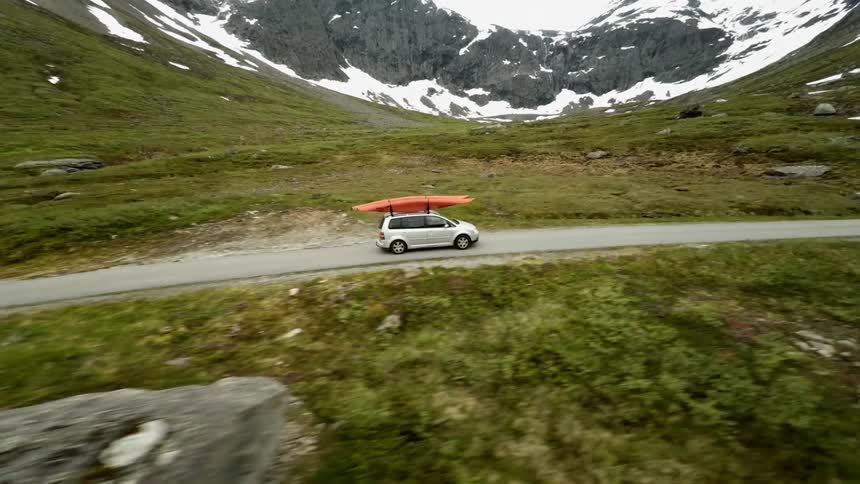 A vehicle with a kayak strapped to its roof drives through the wilderness