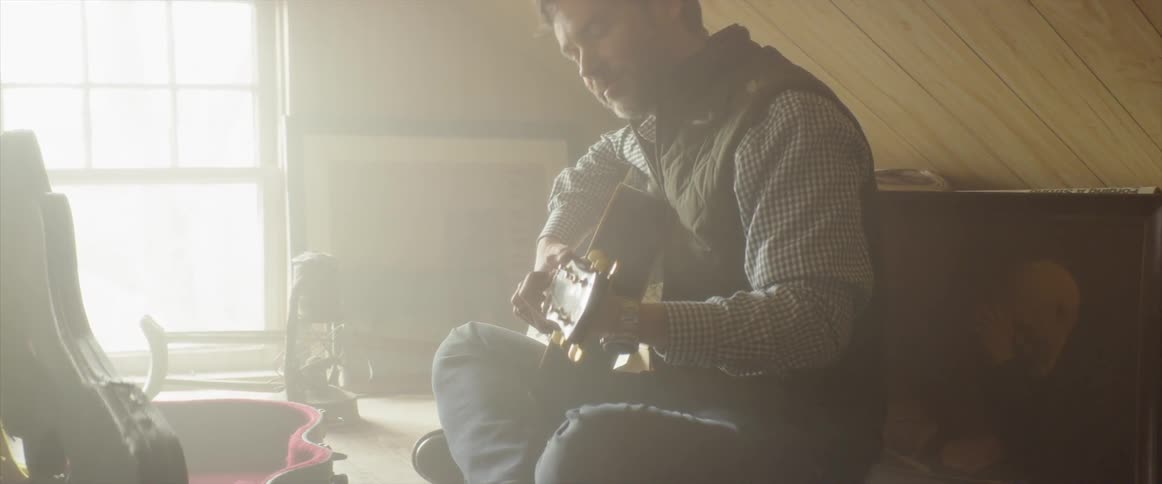 Man is sitting in sunny attic playing guitar