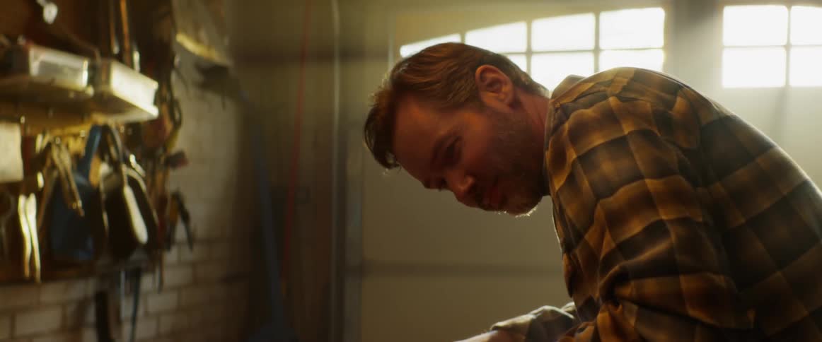 A man is leaning over his work bench