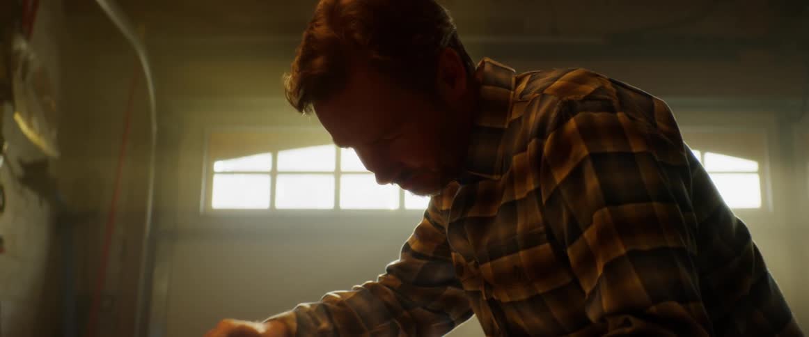 A man is dusting off an object as he stands inside in daylight