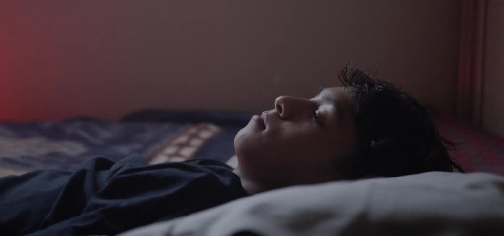 Young boy lays on a bed and blinks his eyes