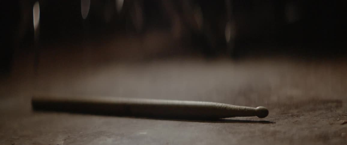 A single drum stick rolls on the ground
