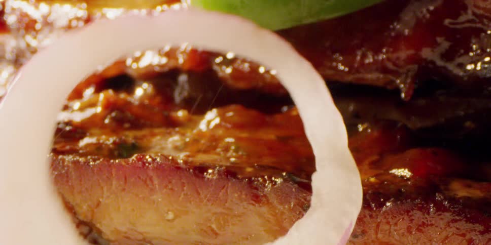 Sliced onions and peppers fall on top of a meat sandwich