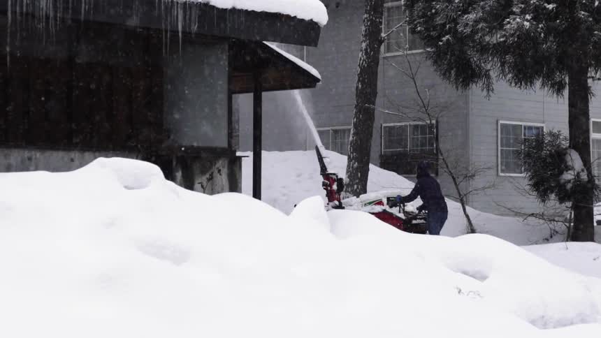 A person is using a snow blower in the yard